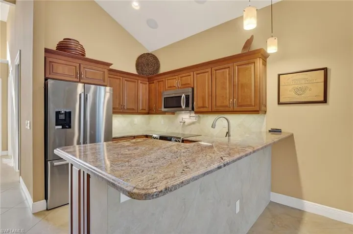 Kitchen with high vaulted ceiling, appliances with stainless steel finishes, a peninsula, brown cabinets, and tasteful backsplash
