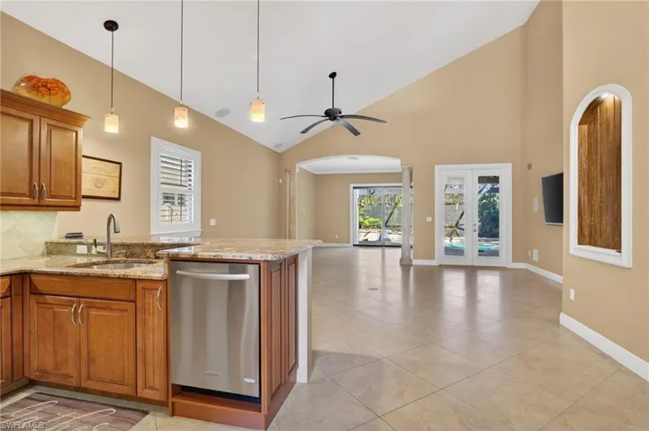 Kitchen with brown cabinetry, light stone counters, stainless steel dishwasher, high vaulted ceiling, and french doors