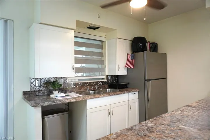 Kitchen with white cabinets, freestanding refrigerator, dark stone counters, a ceiling fan, and decorative backsplash
