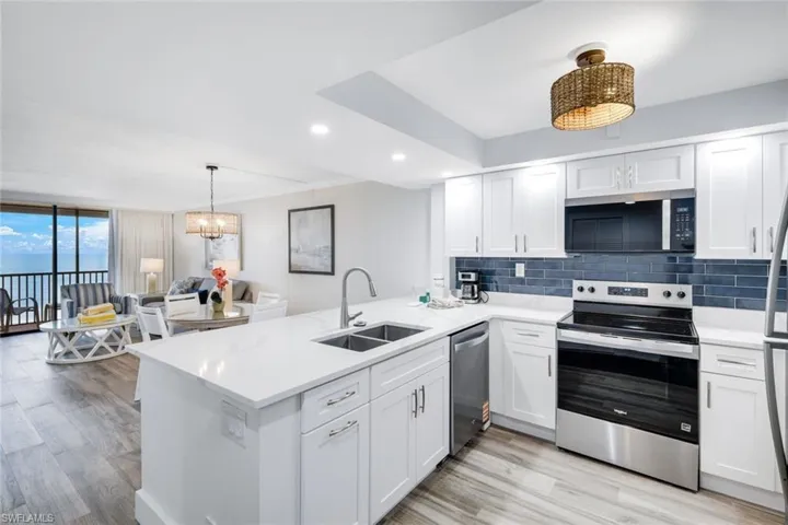 Kitchen featuring stainless steel appliances, white cabinetry, hanging lights, light wood-type flooring, and expansive windows