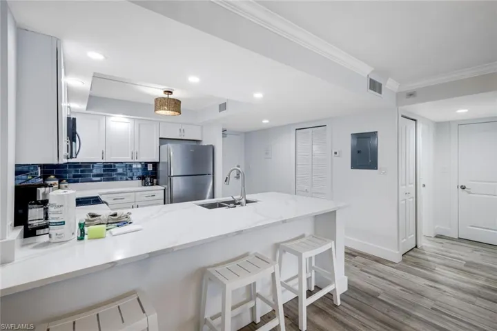 Kitchen featuring a peninsula, a kitchen breakfast bar, white cabinetry, freestanding refrigerator, and tasteful backsplash