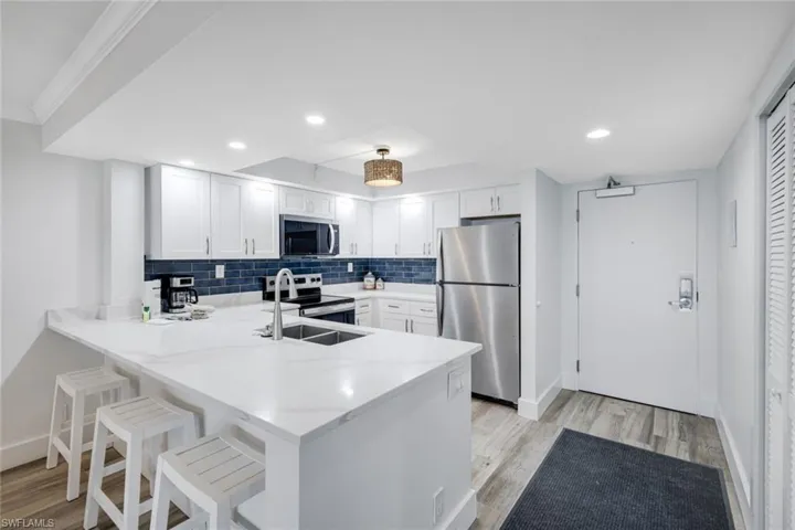 Kitchen featuring a breakfast bar area, a peninsula, white cabinetry, stainless steel appliances, and light stone counters