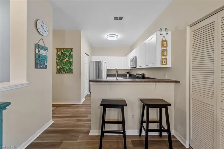 Kitchen with dark countertops, white cabinets, dark wood-style floors, a peninsula, and a breakfast bar area