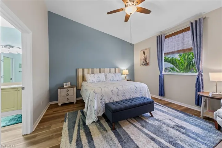 Bedroom with wood finished floors, vaulted ceiling, a ceiling fan, and ensuite bathroom