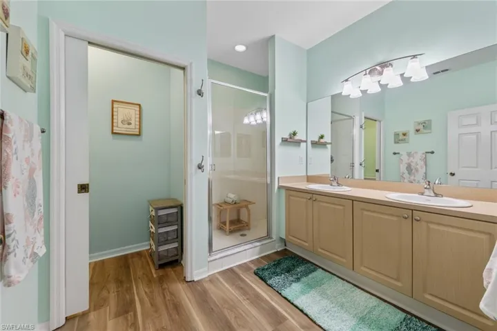 Full bathroom featuring double vanity, light wood-type flooring, and a stall shower