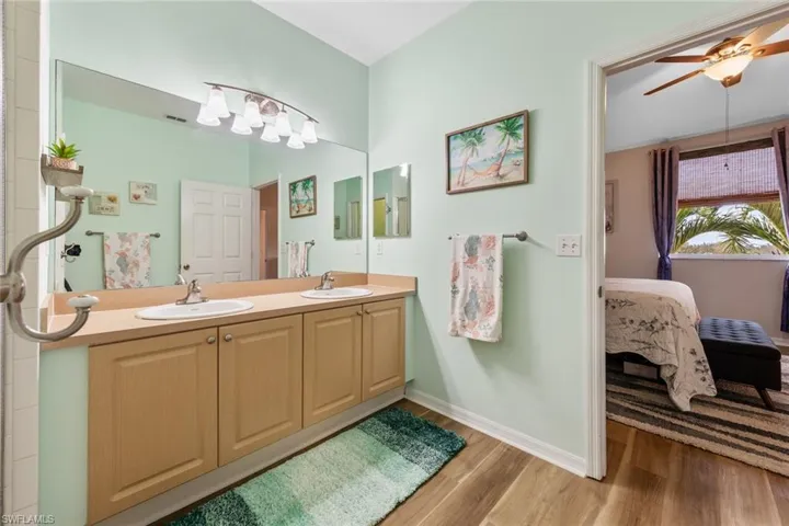 Bathroom featuring light wood-style floors, double vanity, ensuite bath, and ceiling fan