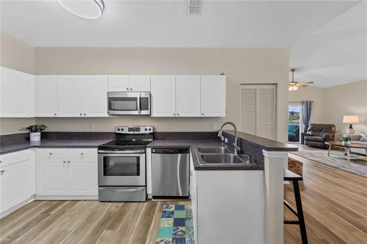 Kitchen featuring appliances with stainless steel finishes, open floor plan, dark countertops, a breakfast bar, and white cabinetry