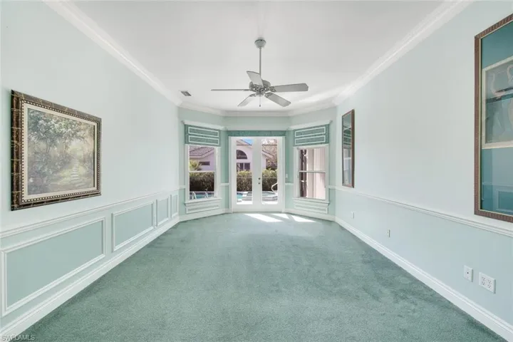 Carpeted empty room featuring french doors, a decorative wall, crown molding, wainscoting, and ceiling fan