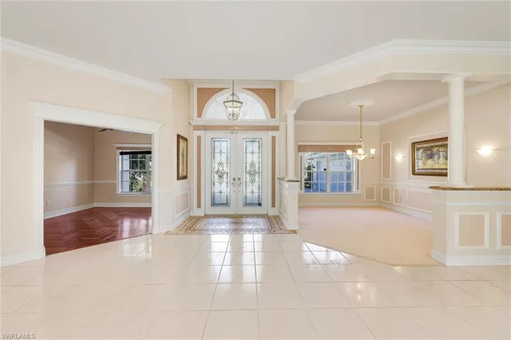 Entrance foyer featuring a chandelier, crown molding, french doors, light tile patterned floors, and decorative columns