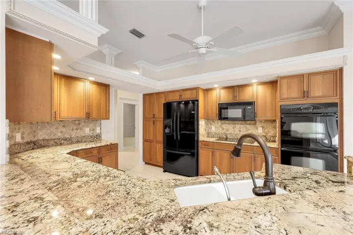 Kitchen with ornamental molding, black appliances, brown cabinets, light stone counters, and recessed lighting