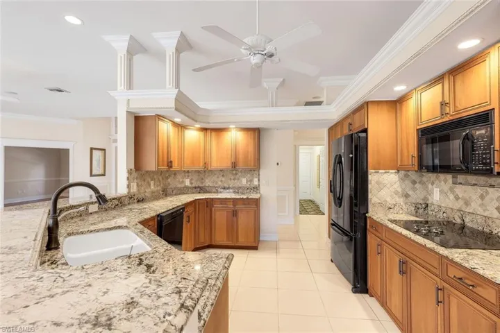 Kitchen with brown cabinetry, black appliances, crown molding, light stone counters, and recessed lighting