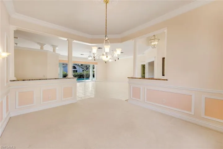 Unfurnished dining area featuring a decorative wall, crown molding, ornate columns, a chandelier, and light colored carpet