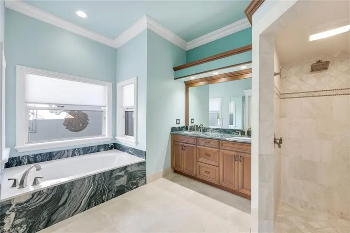 Full bath featuring double vanity, a garden tub, crown molding, recessed lighting, and a stall shower