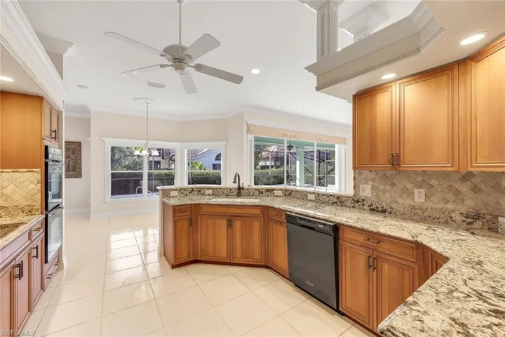 Kitchen featuring decorative backsplash, brown cabinets, crown molding, light stone countertops, and black dishwasher