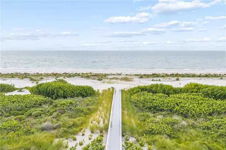 Direct beach access via a private boardwalk, surrounded by lush coastal vegetation, leading to a sandy beach and expansive ocean