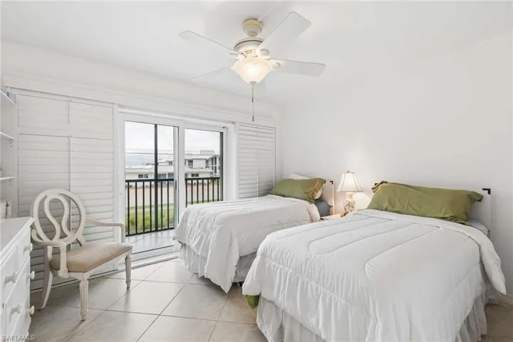 White tiled flooring, sliding glass door leading to a balcony, white plantation shutters.