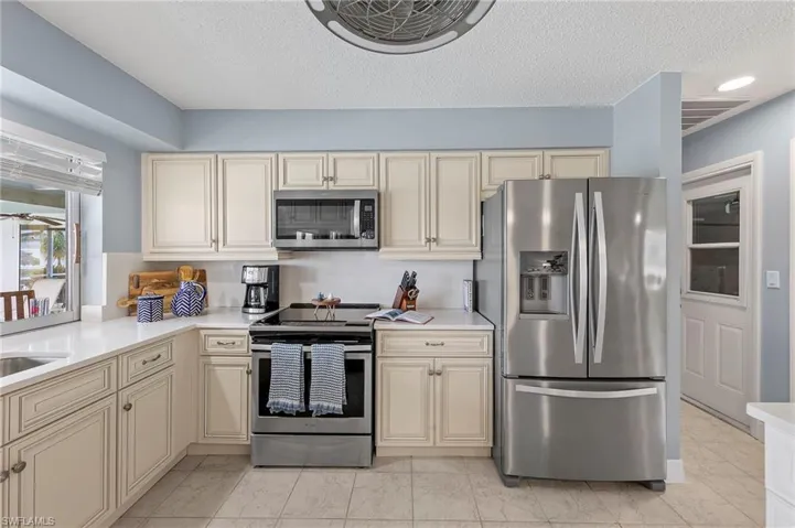 Kitchen featuring a textured ceiling, stainless steel appliances, cream cabinets, and light tile patterned floors