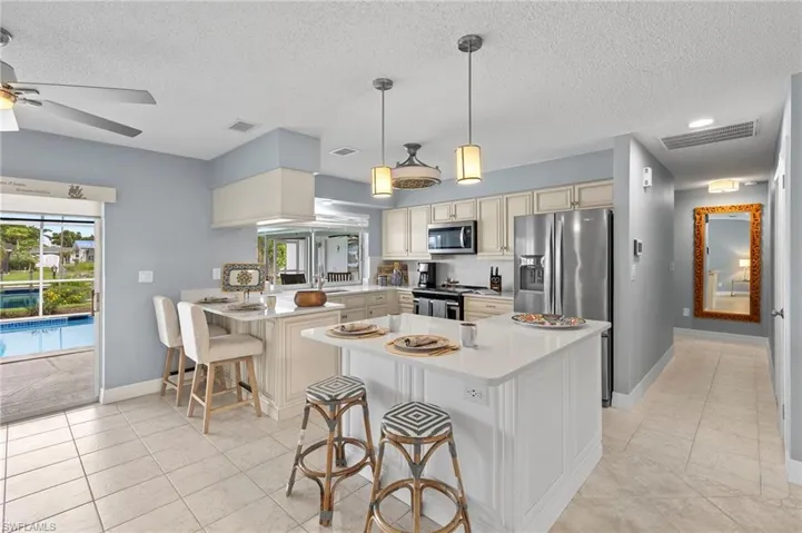 Kitchen with appliances with stainless steel finishes, a kitchen breakfast bar, light tile patterned floors, kitchen peninsula, and ceiling fan