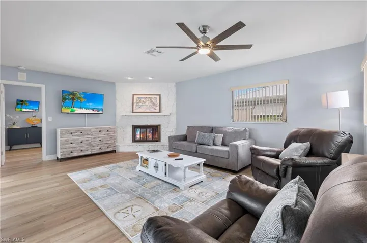 Living room featuring ceiling fan, light wood-type flooring, and a stone fireplace