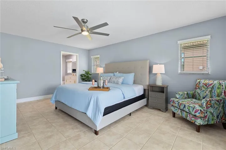 Bedroom with multiple windows, ensuite bathroom, light tile patterned flooring, and ceiling fan