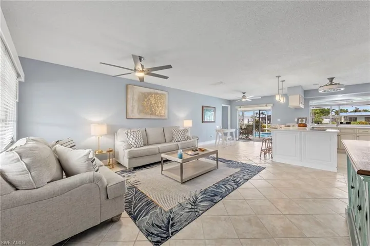 Living room with a textured ceiling, ceiling fan, and light tile patterned flooring