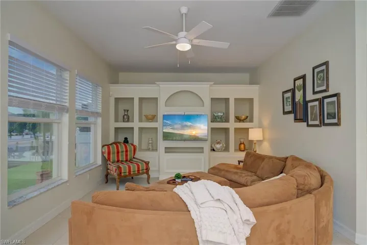 Living area featuring a ceiling fan, light tile patterned flooring, and built in shelves