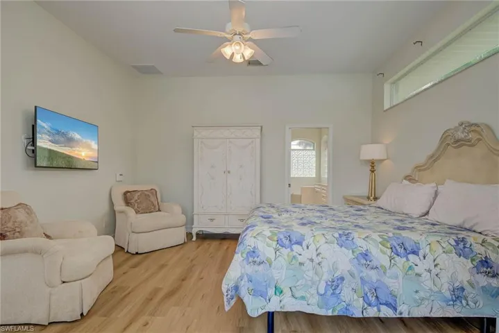Bedroom featuring light wood-style floors, a ceiling fan, ensuite bathroom, and multiple windows
