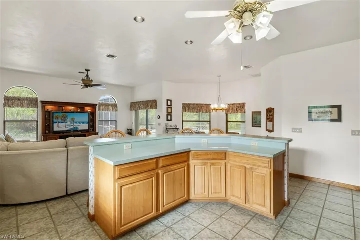 Kitchen with light tile patterned floors, pendant lighting, ceiling fan with notable chandelier, and a kitchen island with sink