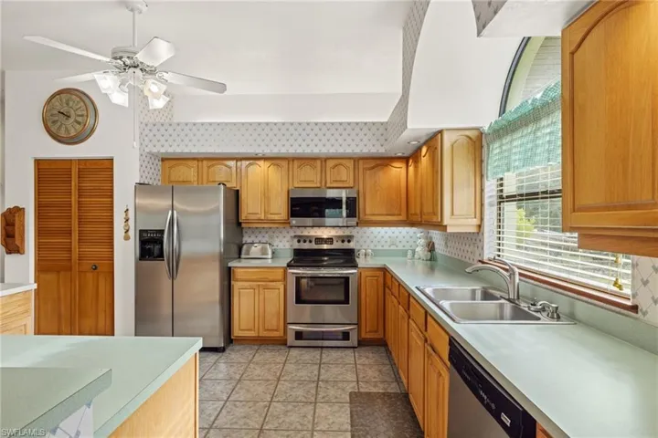 Kitchen featuring ceiling fan, appliances with stainless steel finishes, backsplash, light tile patterned flooring, and sink