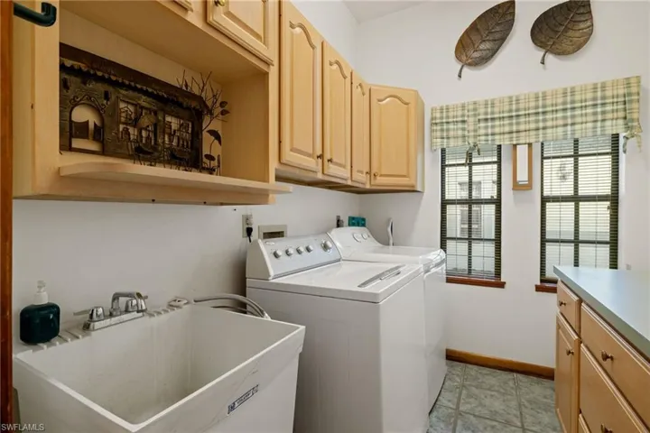 Laundry room with sink, washing machine and clothes dryer, light tile patterned floors, and cabinets