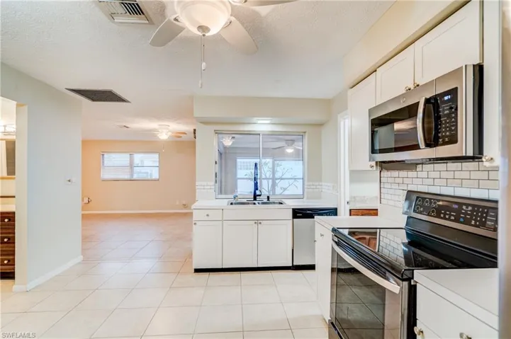 Kitchen featuring ceiling fan, light tile patterned floors, sink, white cabinets, and stainless steel appliances