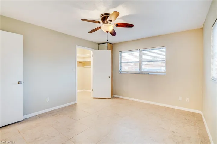 Unfurnished bedroom featuring a closet, light tile patterned floors, ceiling fan, and a walk in closet