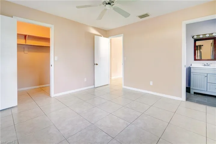 Unfurnished bedroom featuring a walk in closet, light tile patterned floors, ceiling fan, and ensuite bathroom
