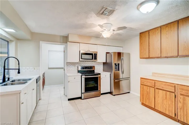 Kitchen featuring ceiling fan, appliances with stainless steel finishes, white cabinetry, sink, and backsplash