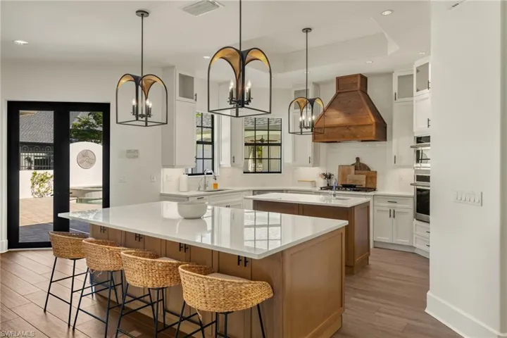 Kitchen with premium range hood, a kitchen island with sink, white cabinetry, and plenty of natural light