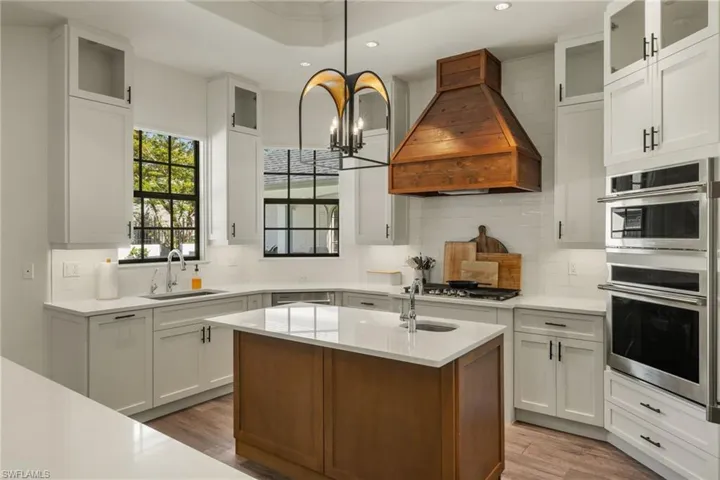 Kitchen featuring white cabinets, sink, premium range hood, and a kitchen island with sink
