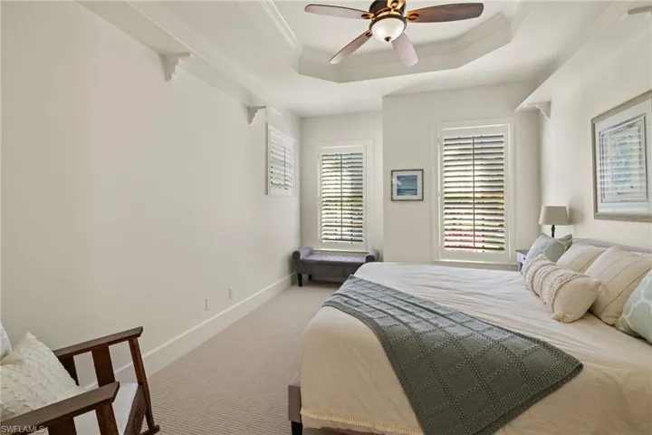 Carpeted bedroom with ceiling fan, ornamental molding, and a tray ceiling