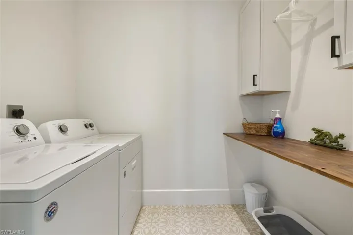 Upstairs laundry room with washer and clothes dryer, light tile patterned flooring, and cabinets