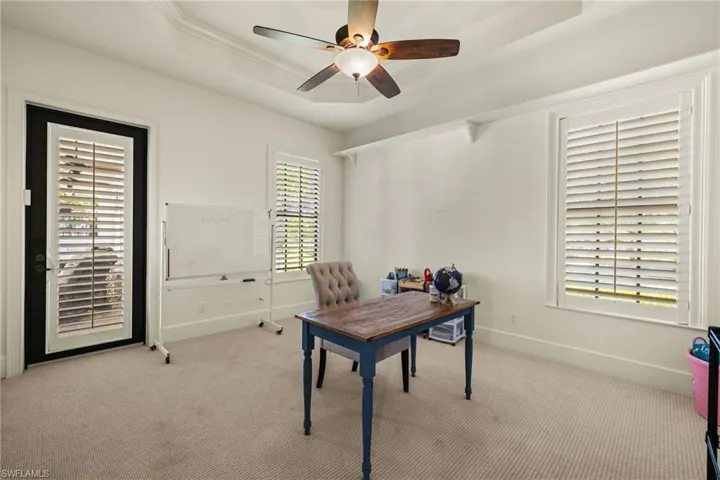 Carpeted office featuring a raised ceiling, ceiling fan, and ornamental molding