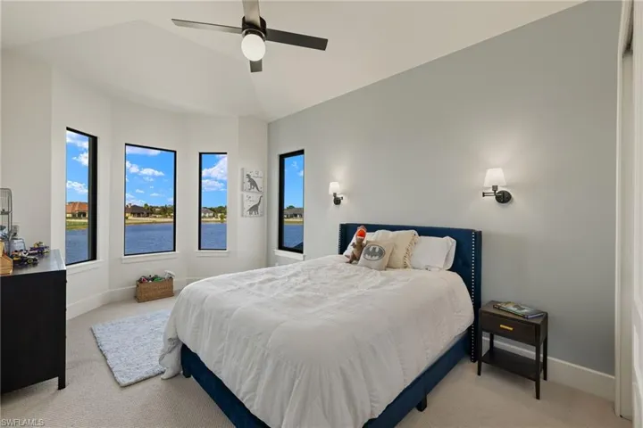 Bedroom with ceiling fan, a water view, light carpet, and vaulted ceiling