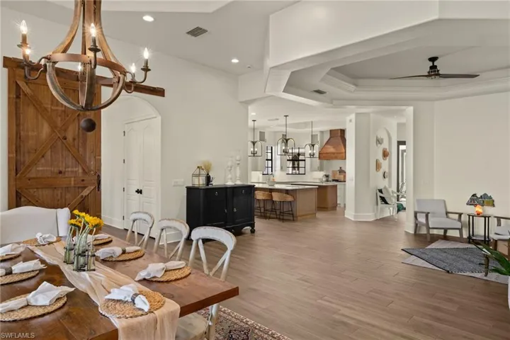 Dining room featuring ceiling fan with notable chandelier, hardwood / wood-style floors, a barn door, and a tray ceiling