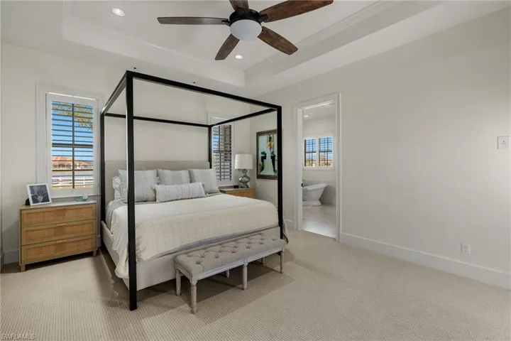 Carpeted bedroom with ceiling fan, a raised ceiling, crown molding, and connected bathroom