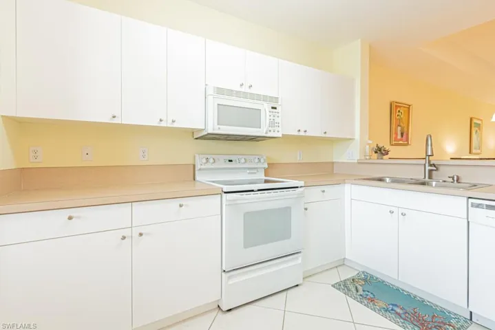 Kitchen featuring white appliances, light tile patterned floors, white cabinets, and light countertops