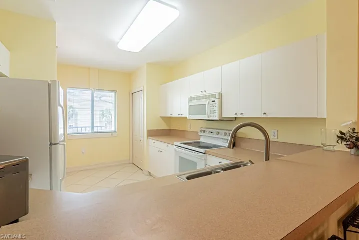 Kitchen featuring white appliances, light countertops, light tile patterned flooring, a peninsula, and white cabinetry