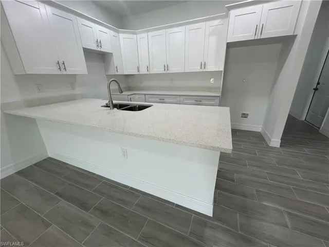 Kitchen with a peninsula, white cabinets, light stone counters, and wood tiled floors