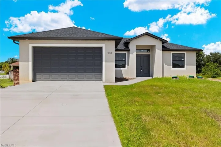 View of front of home with an attached garage, a front yard, driveway, stucco siding, and roof with shingles