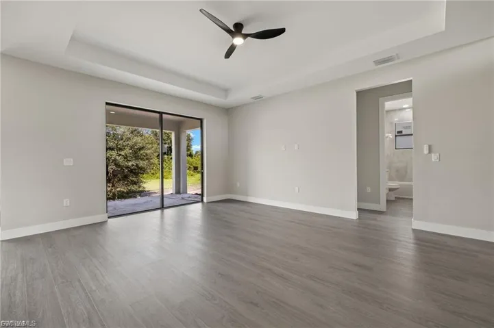 Empty room with a tray ceiling, a ceiling fan, and dark wood-style flooring