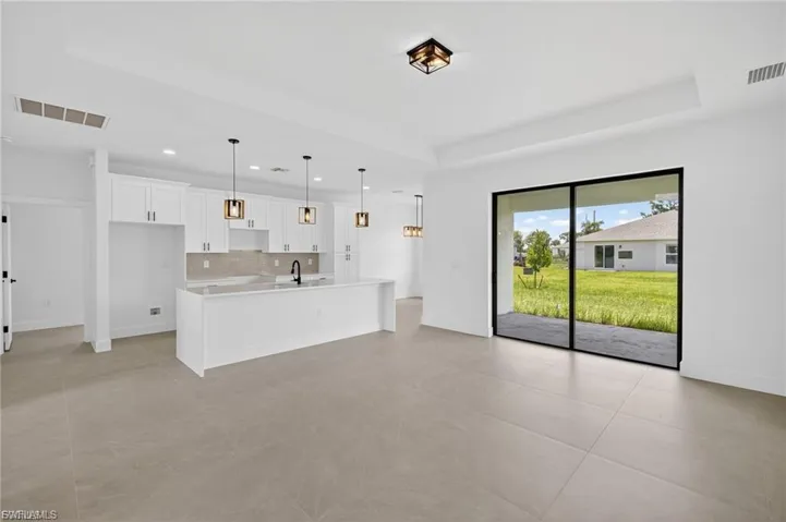 Kitchen featuring white cabinetry, a raised ceiling, open floor plan, pendant lighting, and a kitchen island with sink