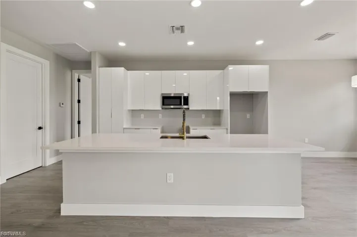 Kitchen with an island with sink, recessed lighting, white cabinetry, light wood-style flooring, and stainless steel microwave