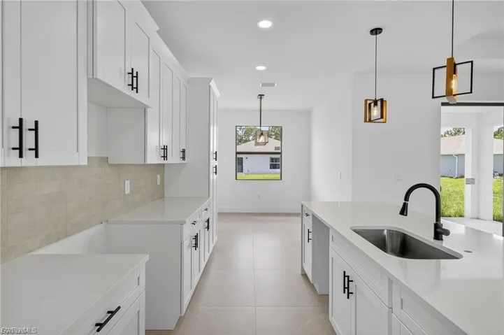 Kitchen with white cabinetry, light stone countertops, decorative light fixtures, and backsplash